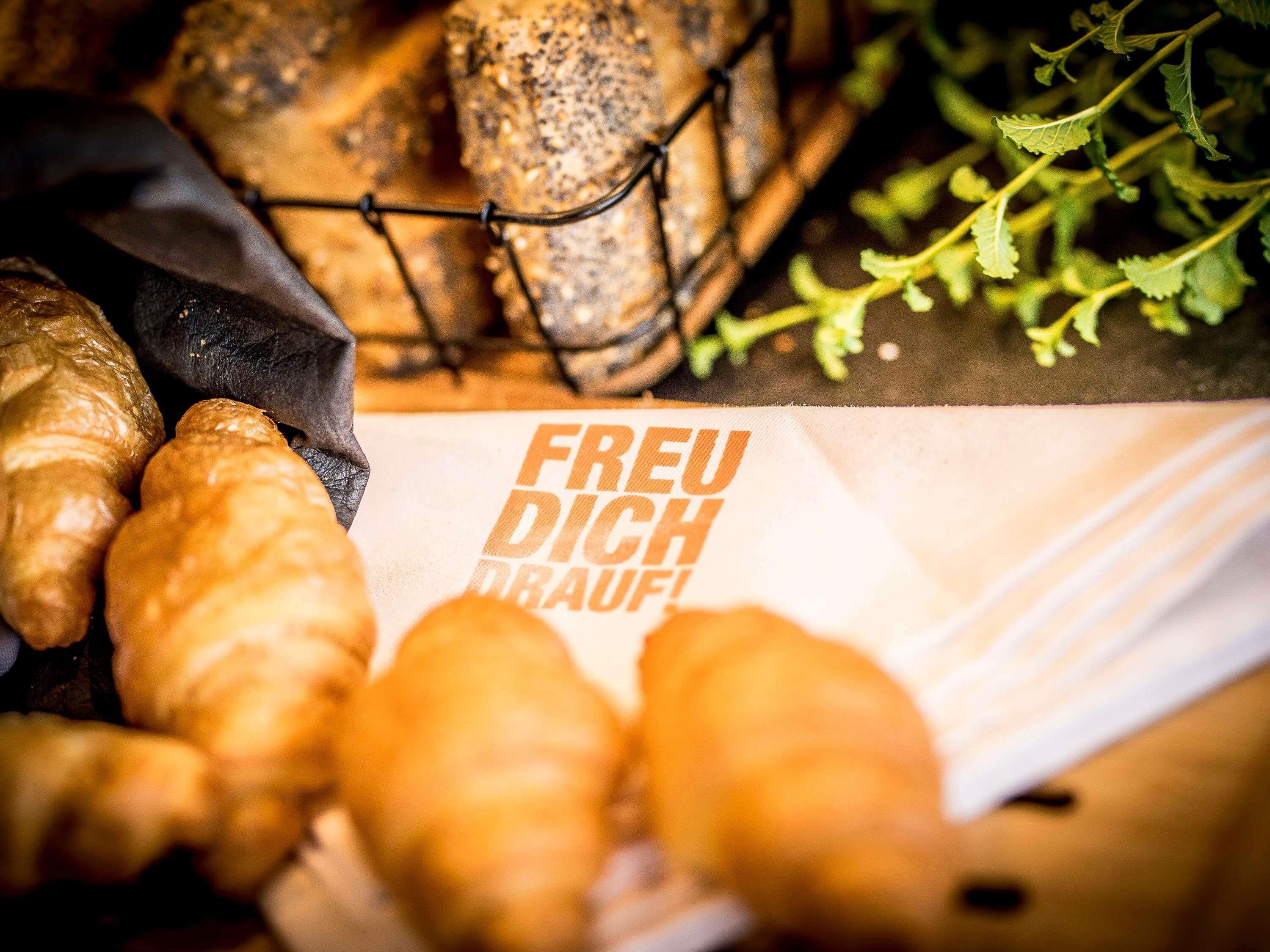 A variety of baked goods, including croissants and bread, with a paper bag labeled 'FREU DICH TRAUFI' partially visible.