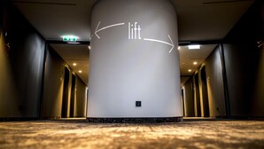 A modern hotel lobby with a central column, directional arrows, and a carpeted floor. - Ibis Wels (Wels)