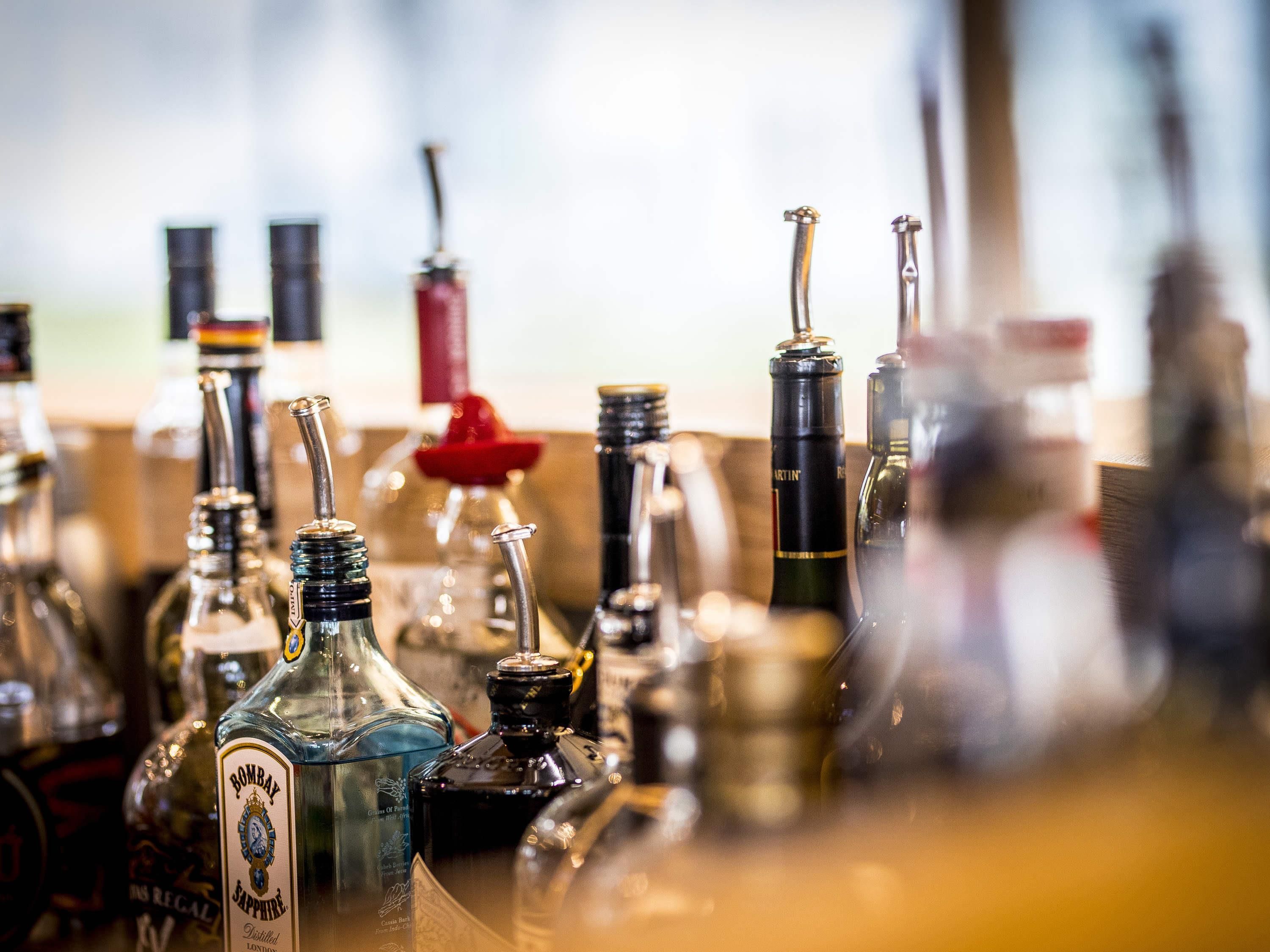 A variety of bottles on a shelf, including a prominent bottle labeled 'Bombay Sapphire.'