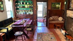 Un comedor con una mesa de madera, sillas y un banco. Hay una estantería con vajilla y un cuadro en la pared.