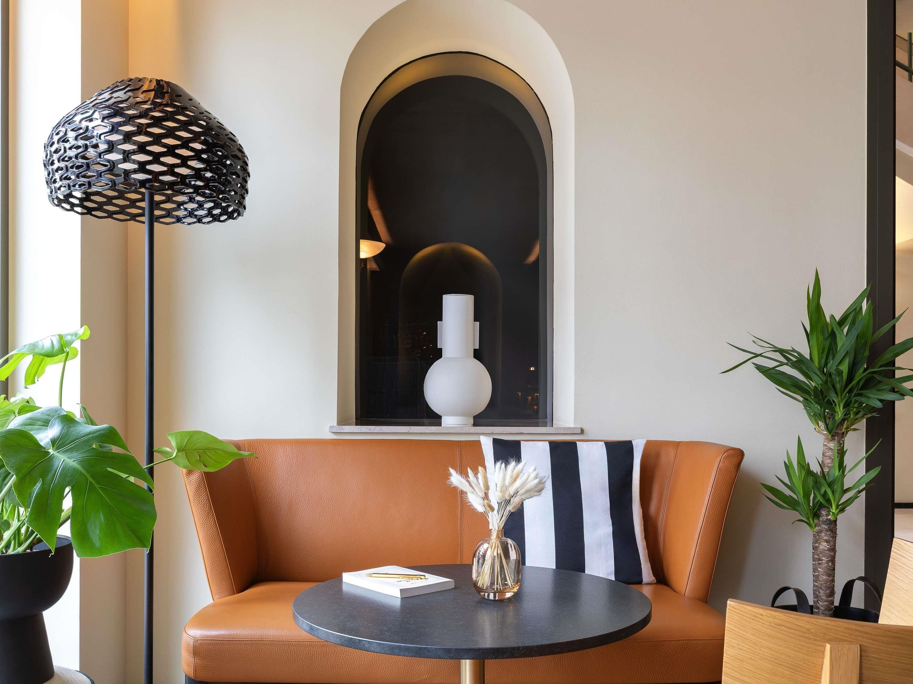 Una sala de estar moderna con un sofá de cuero, una mesa redonda, una planta en maceta y una lámpara negra original.