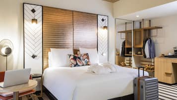 Quarto de hotel com cama, escrivaninha, laptop, mala e guarda-roupa.