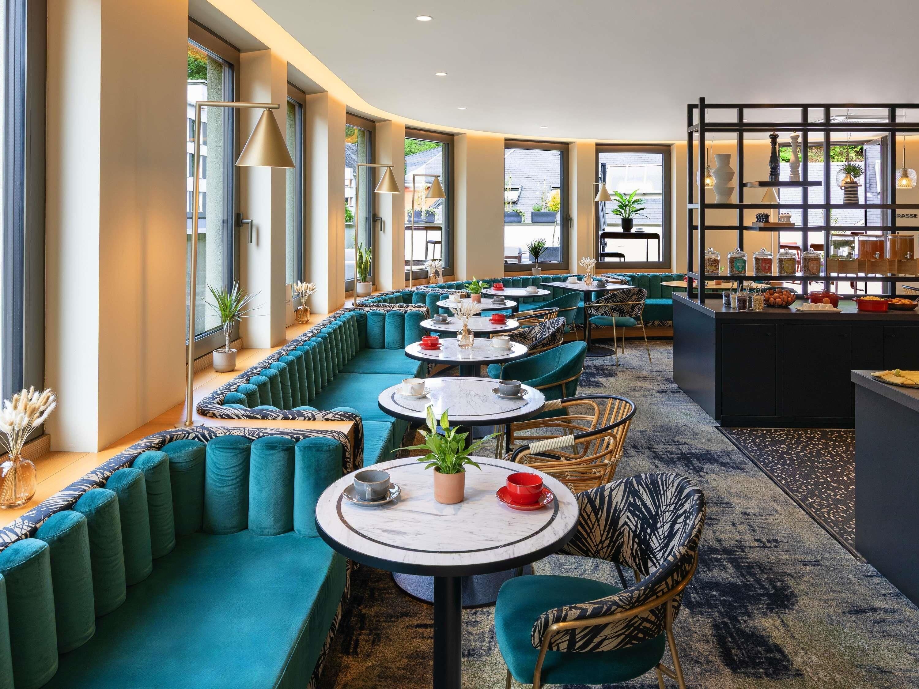 Um restaurante moderno com assentos tons de verde-água, mesas redondas e uma área de buffet.