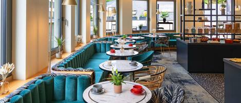 En modern restaurang med turkosa sittplatser, runda bord och ett område med buffé.