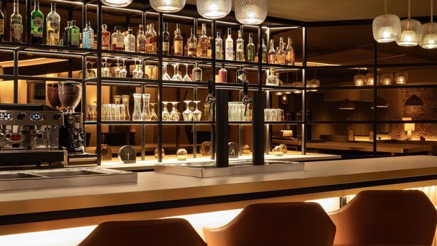 A bar area with shelves of liquor bottles, glasses, and a coffee machine. - Mercure Luxembourg off Kirchberg (Luxembourg City)