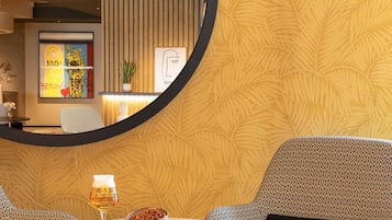 A modern interior with a round table, two patterned chairs, a glass of beer, and a bowl of pretzels.