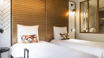 A hotel room with two beds, a wooden headboard, a mirror, and a bedside table with a lamp.