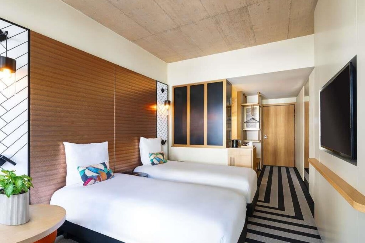 Een hotelkamer met twee bedden, een televisie, een houten hoofdbord, een potplant en een gestreept tapijt.