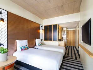 Een hotelkamer met twee bedden, een televisie, een houten hoofdbord, een potplant en een gestreept tapijt.