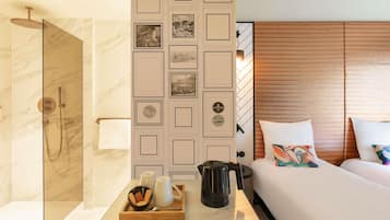 A hotel room with a shower, a bed with pillows, a bedside table with a tray of toiletries, and a decorative wall panel.