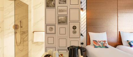 A hotel room with a shower, a bed with pillows, a bedside table with a tray of toiletries, and a decorative wall panel.