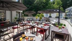 An outdoor patio with tables and chairs, umbrellas, and a breakfast tray. - Mercure Luxembourg off Kirchberg (Luxembourg City)