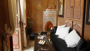 A cozy living room with a fireplace, a sofa, and a coffee table. - Riad Teranga (Marrakech)
