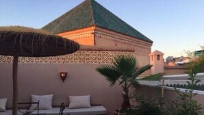 A building with a green-tiled roof, a decorative wall, and a seating area with cushions. - Riad Teranga (Marrakech)