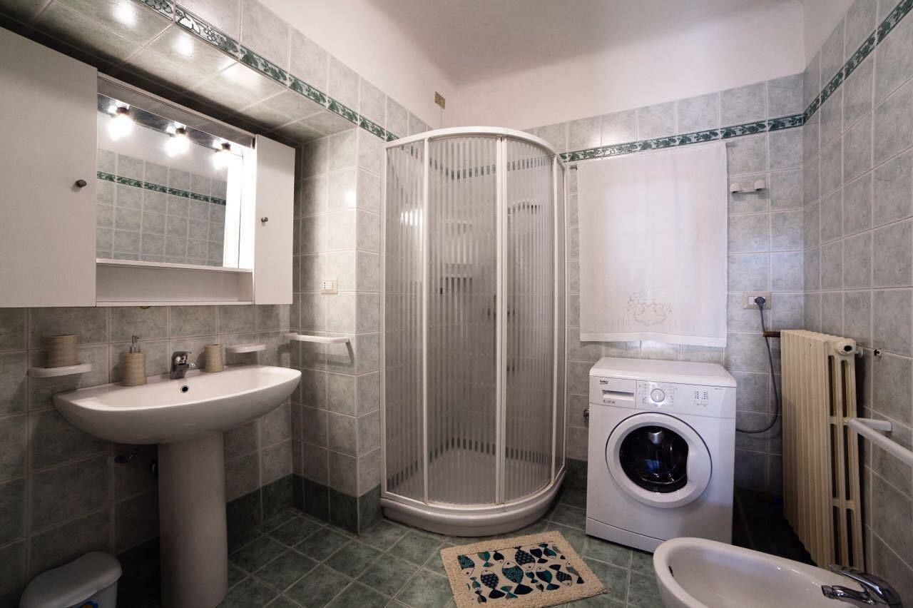 Un bagno con cabina doccia, lavandino, lavatrice e WC.