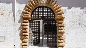 A stone archway with a metal gate, leading to a building with a white wall. - La corte dei mille (Presicce-Acquarica)