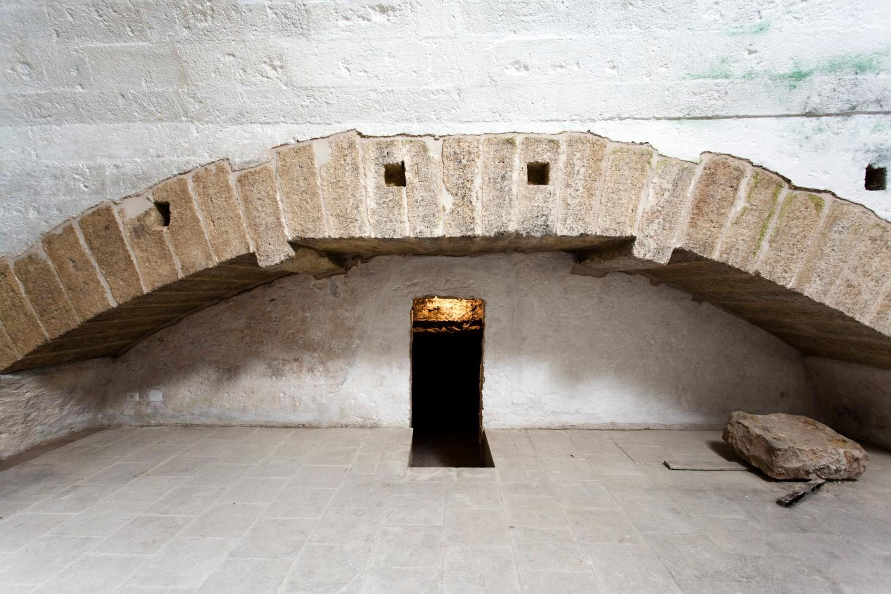 Una stanza con soffitto a volta, una piccola finestra e un muro in pietra.