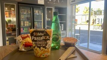 Un vassoio con una confezione di Sodebo PastaBox, una bottiglia d'acqua Perrier e un piccolo contenitore di salsa, appoggiato su un tavolo in un negozio con un cartello Mini Comptoir.