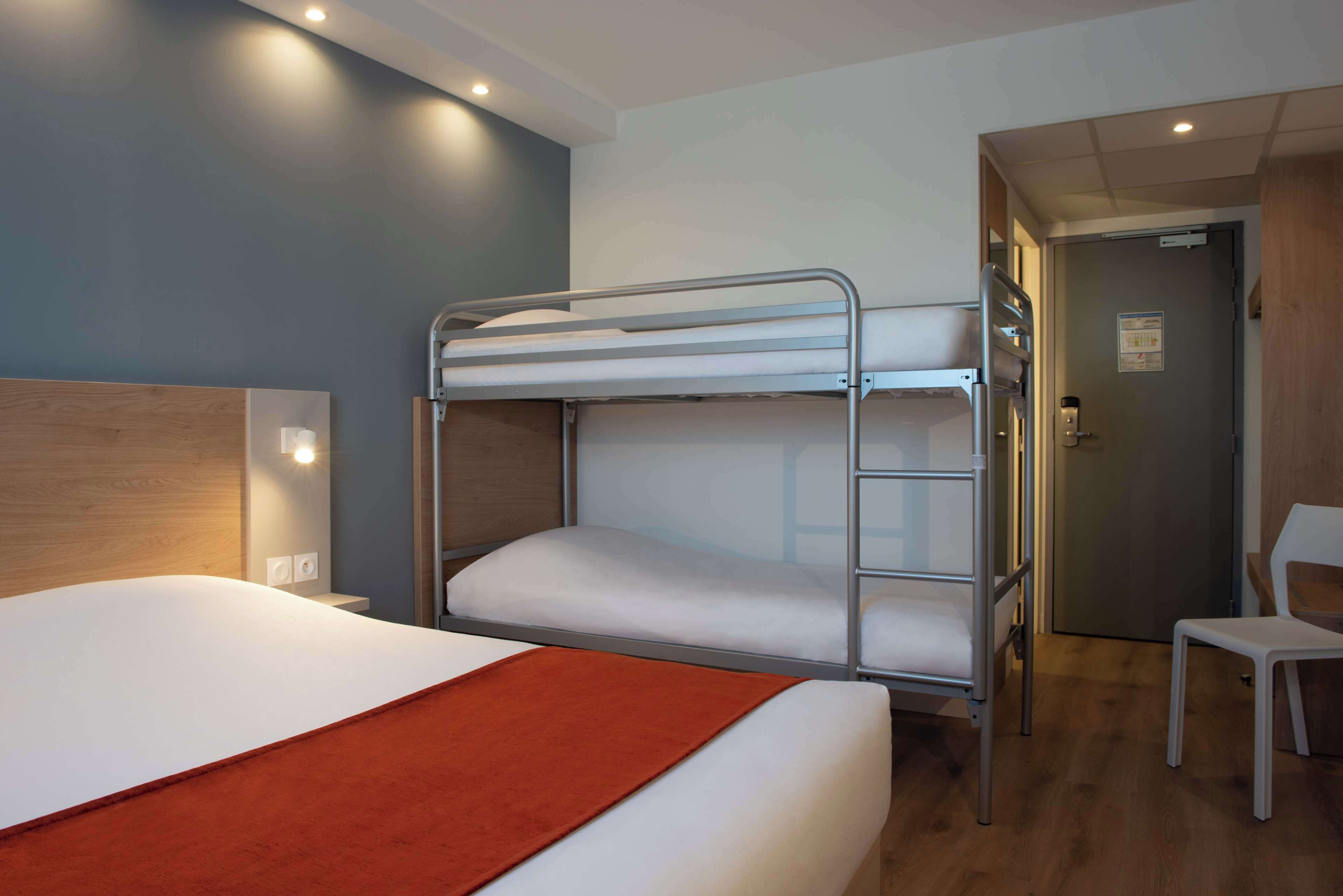 Een slaapkamer met een stapelbed, een enkel bed, een stoel en een deur.