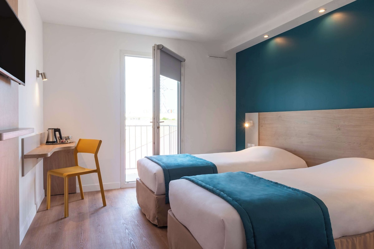 Ein Hotelzimmer mit zwei Betten, einem Schreibtisch mit Stuhl und einem großen Fenster.