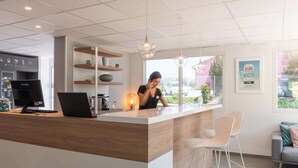Ein moderner Empfangsbereich mit einem Holzboden, einem Computer und einer Kaffeemaschine. Regale mit Dekorationselementen und ein Fenster mit Blick ins Freie.