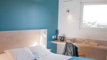 Ett hotellrum med en säng, ett skrivbord, en stol och ett fönster.
