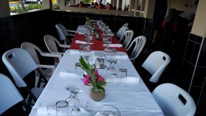 Um restaurante com uma longa mesa de jantar posta para uma refeição, rodeada por cadeiras brancas.