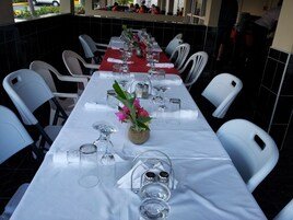 A restaurant with a long dining table set for a meal, surrounded by white chairs.