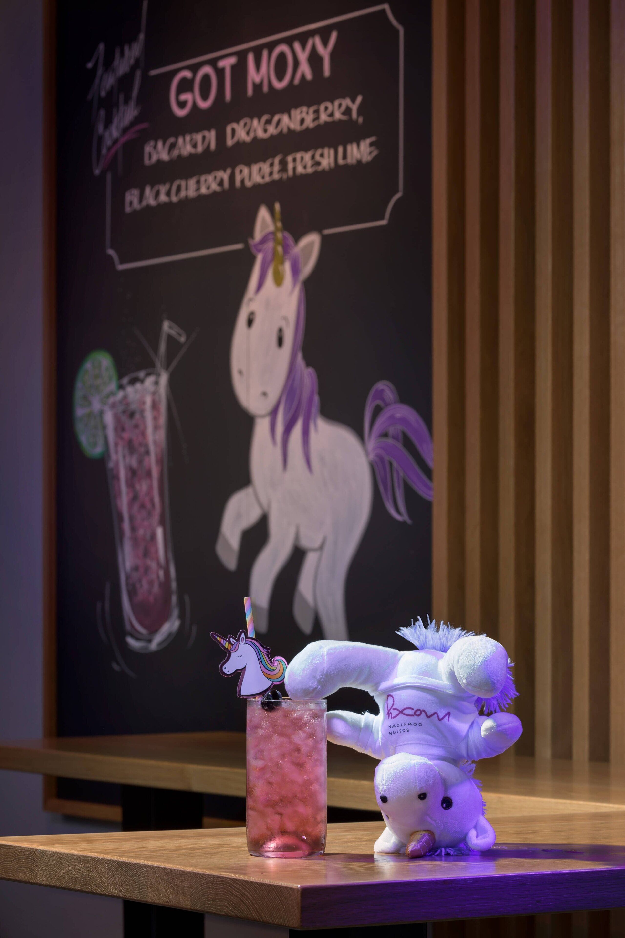 Una ilustración de un unicornio, una bebida con pajita de unicornio y un peluche sobre una mesa de madera.