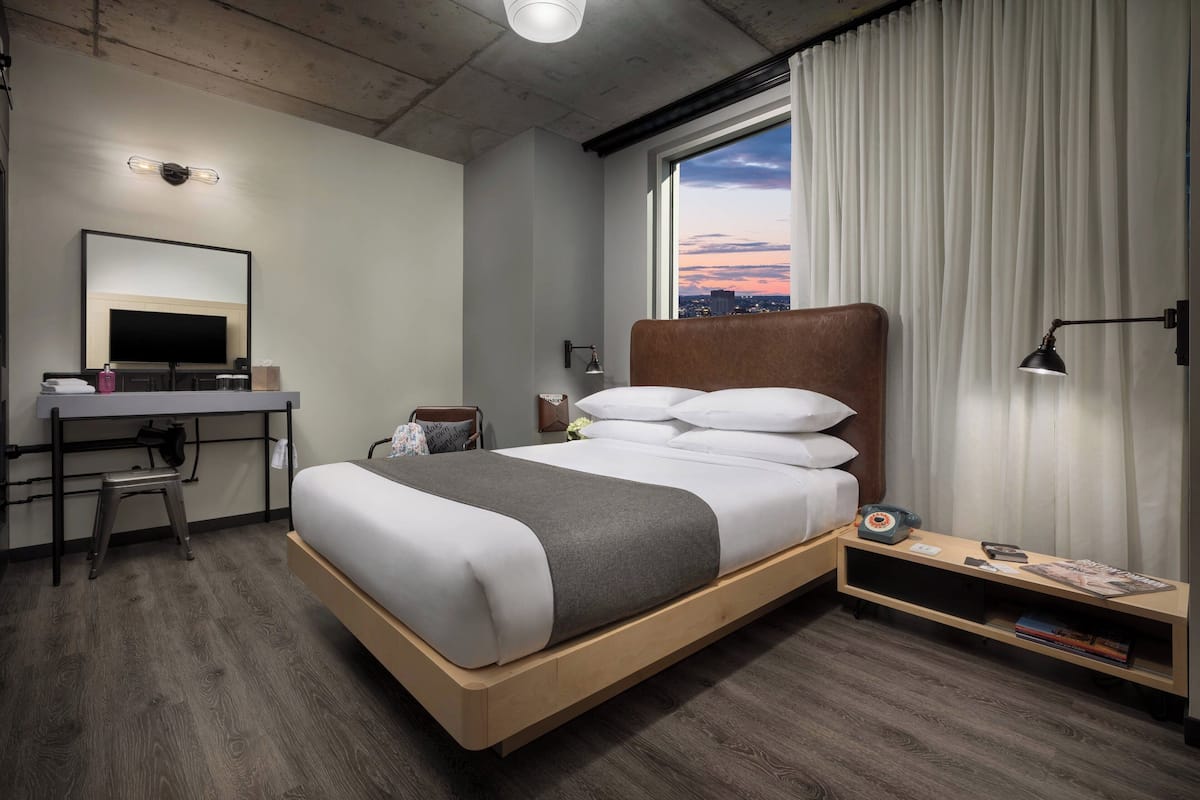 A modern hotel room with a bed, desk, and a city view.