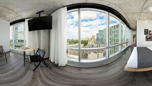 Une vue panoramique depuis une chambre située dans un immeuble de grande hauteur, avec une fenêtre incurvée, un téléviseur à écran plat, une petite table ronde et une chaise noire.
