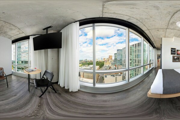 Une vue panoramique depuis une chambre située dans un immeuble de grande hauteur, avec une fenêtre incurvée, un téléviseur à écran plat, une petite table ronde et une chaise noire.
