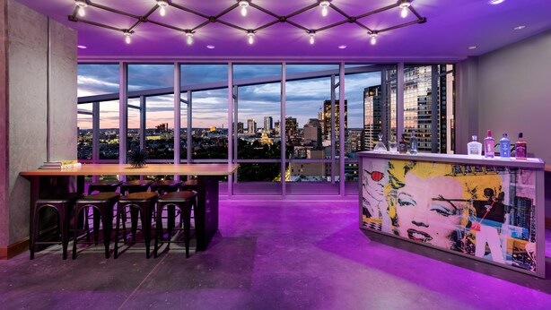 Un espace bar moderne offrant une vue sur la ville, de grandes fenêtres et un comptoir avec des tabourets.