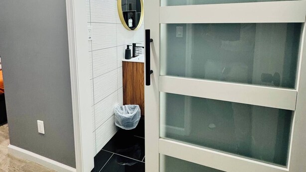 Un baño moderno con puerta de vidrio corredera, un espejo con marco dorado y una pequeña tocador de madera.