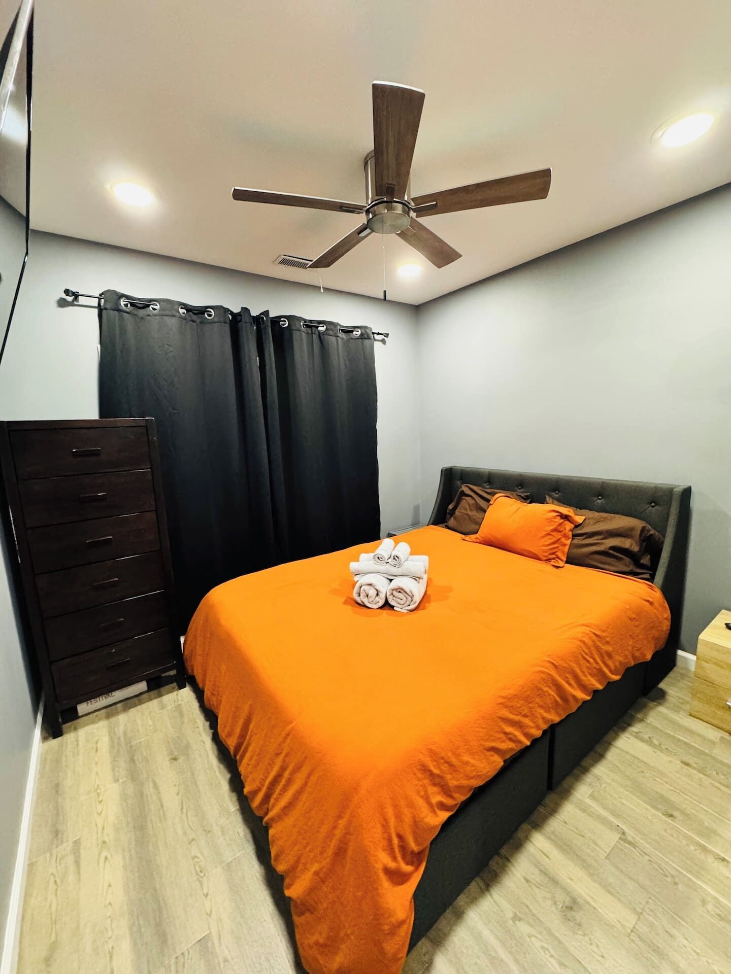 Un dormitorio con cama, cómoda, ventilador de techo y cortina.