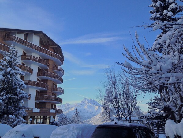 A multi-story building with balconies, surrounded by snow-covered trees and mountains in the background.