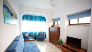 A living room with a sofa, a TV on a wooden stand, a cabinet, and a window with curtains. - Meriteluna Sky Sintra (Sintra)