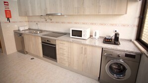 A compact kitchen with wooden cabinets, a built-in microwave, a coffee maker, and a washing machine. - Meriteluna Sky Sintra (Sintra)