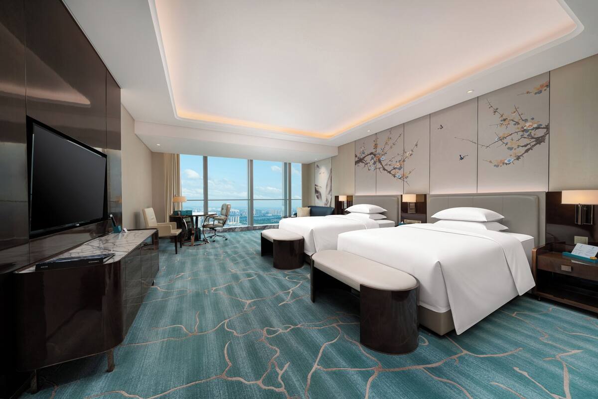 A hotel room with a large TV, two beds, a desk, and a view of the city.