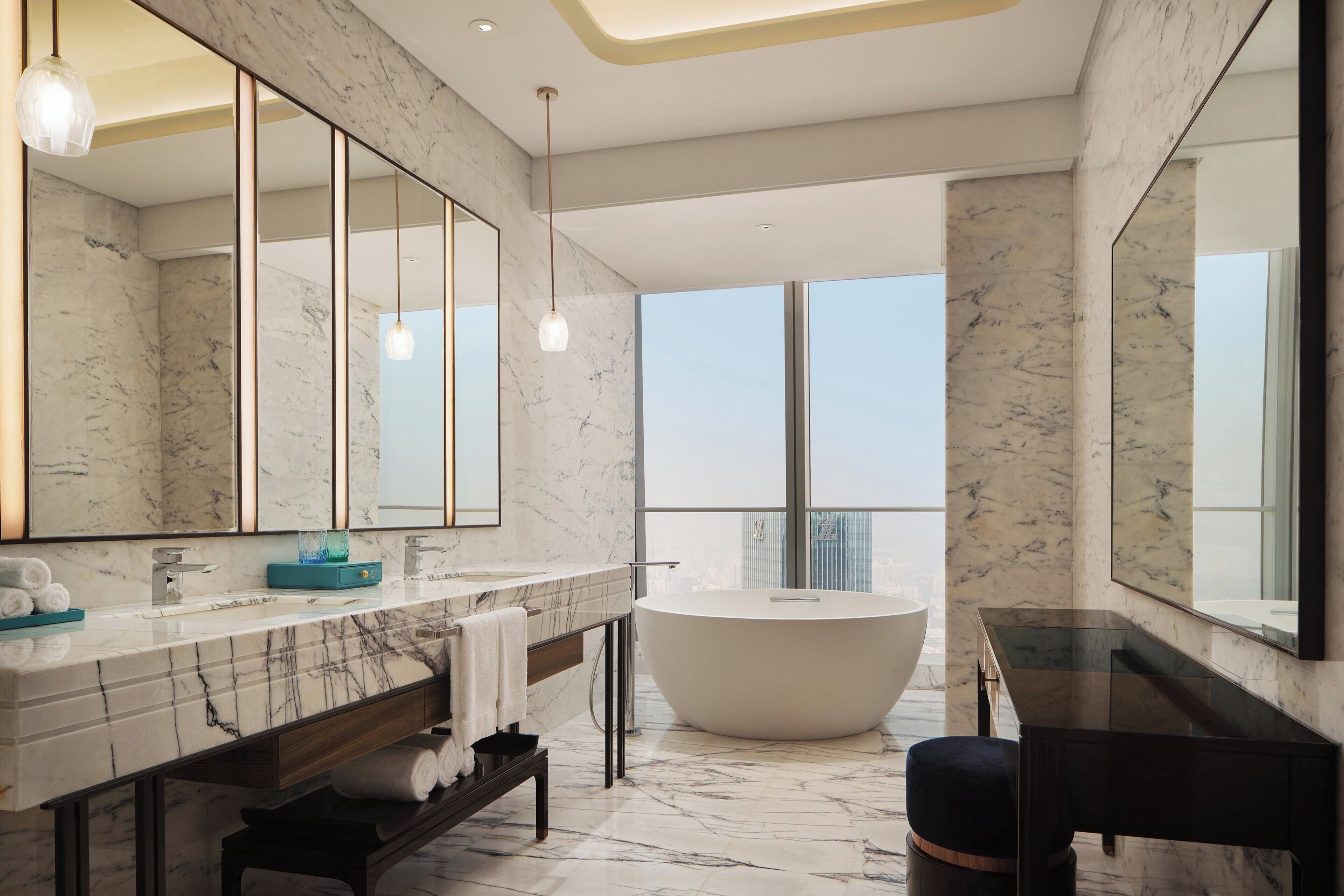 Une salle de bain moderne dotée d’un grand miroir, de plans de travail en marbre, d’une baignoire sur pieds et offrant une vue sur la ville.