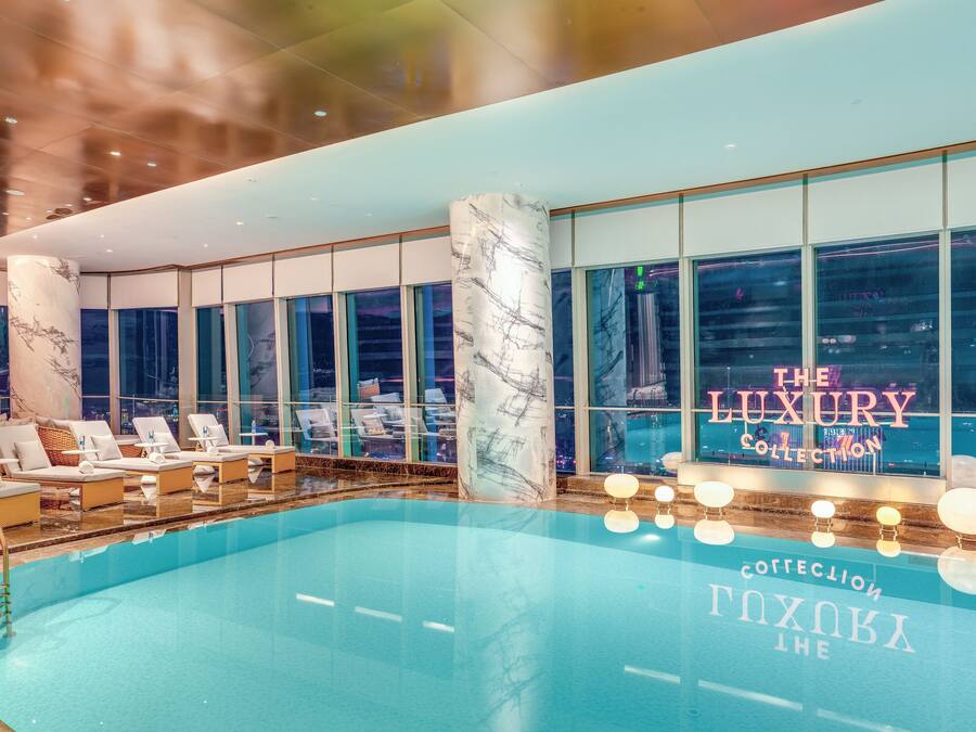 A luxurious indoor pool area with a view of the cityscape, large windows, and modern furnishings.