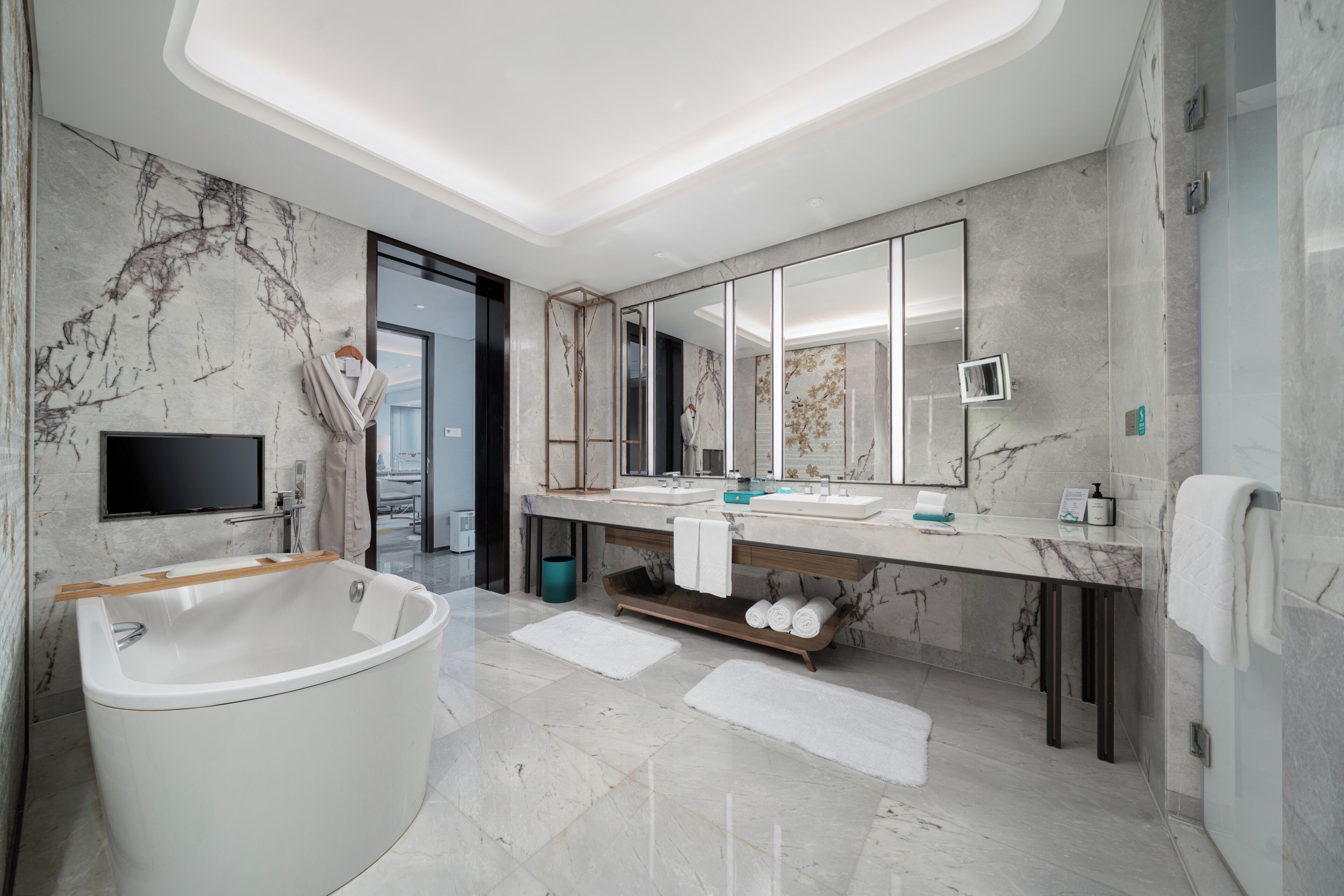 A modern bathroom with a freestanding bathtub, a large mirror, and a marble-tiled floor.