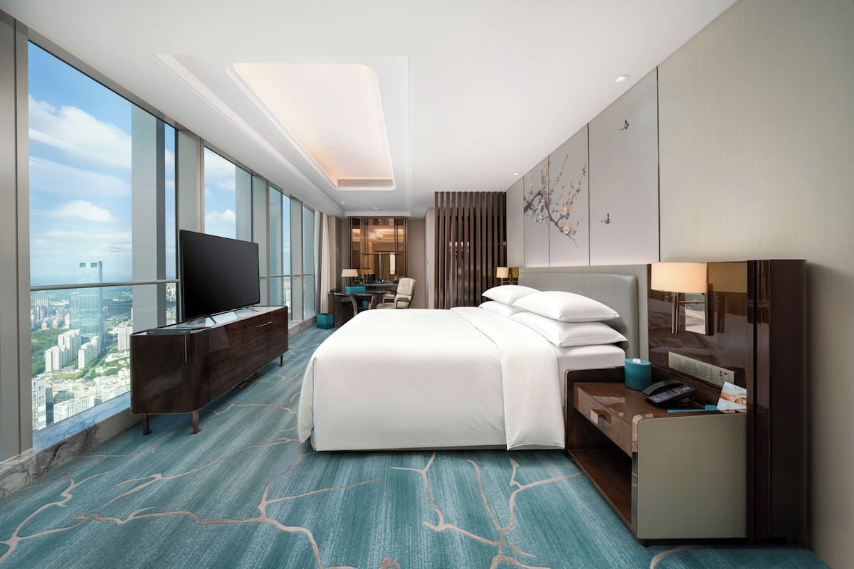A hotel room with a large bed, a TV, a desk, and a view of the city.
