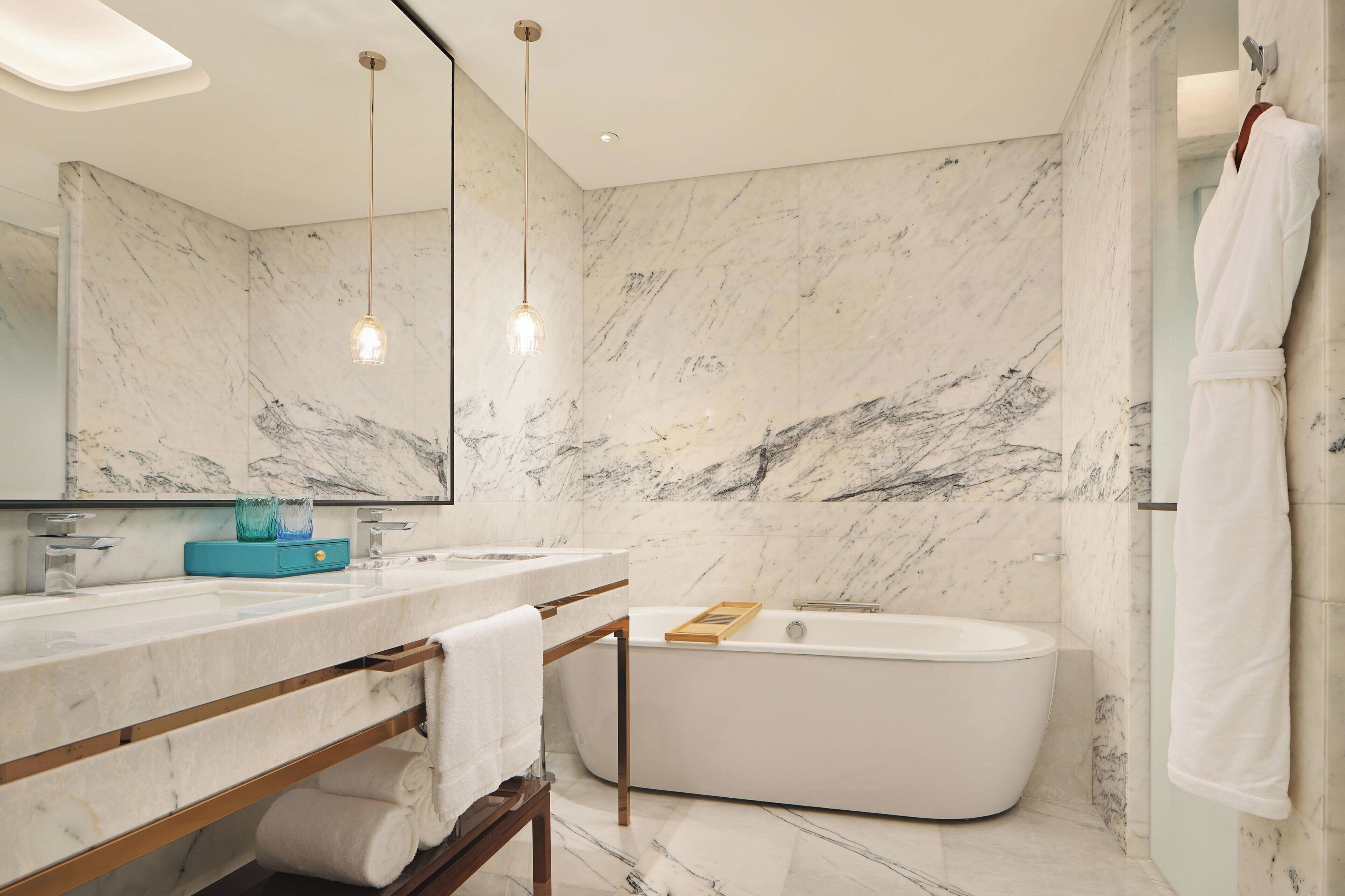 A modern bathroom with a marble wall, a bathtub, a vanity with a mirror, and hanging lights.