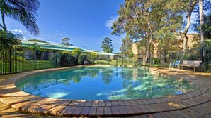 A swimming pool with a brick border, surrounded by a fence, trees, and a bench. - Bay Parklands, 28/2 Gowrie Ave - pool, tennis + stunning views (Nelson Bay)