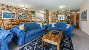 A living room with two blue sofas, a wooden coffee table, and a patterned rug. - Bay Parklands, 28/2 Gowrie Ave - pool, tennis + stunning views (Nelson Bay)