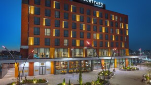 Un hotel Courtyard by Marriott con fachada de ladrillo moderno, ventanas amplias y un área exterior bien iluminada con mobiliario y plantas.