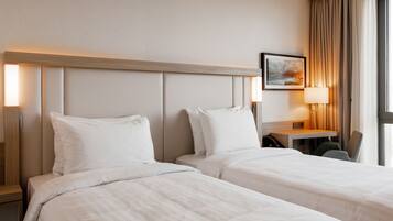 A hotel room with two beds, a desk, a chair, and a lamp.