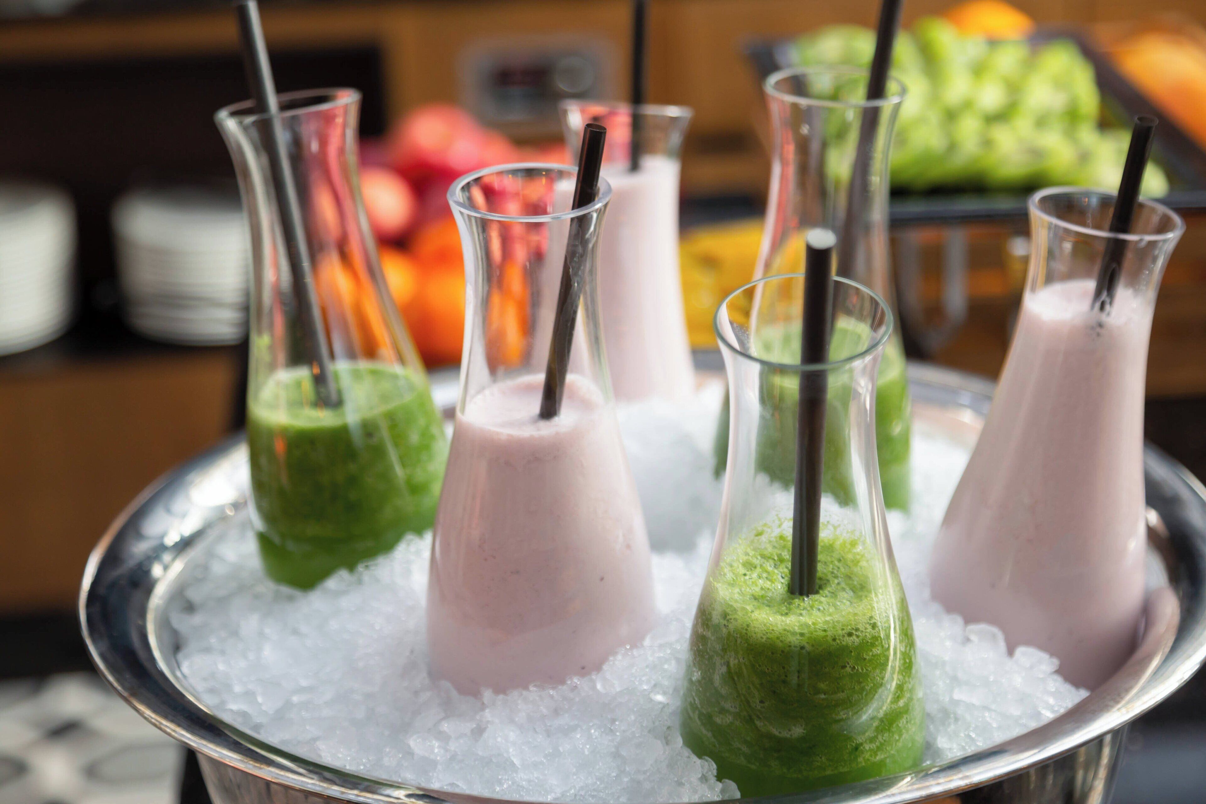 A tray of smoothies in glass bottles with straws, placed on ice.
