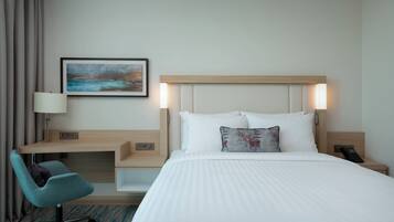 Habitación de hotel con cama, escritorio, silla, un cuadro y mesita de noche con teléfono.